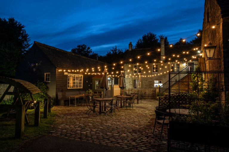Nighttime, fairy ligts over the cobbled stones and benches in the White Hart Ford outdoor area.